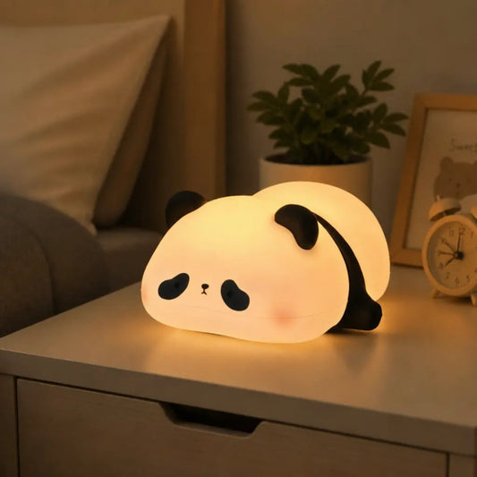 A cute, glowing LED night light shaped like a sleeping panda resting on a bedside table in a cozy bedroom setting.